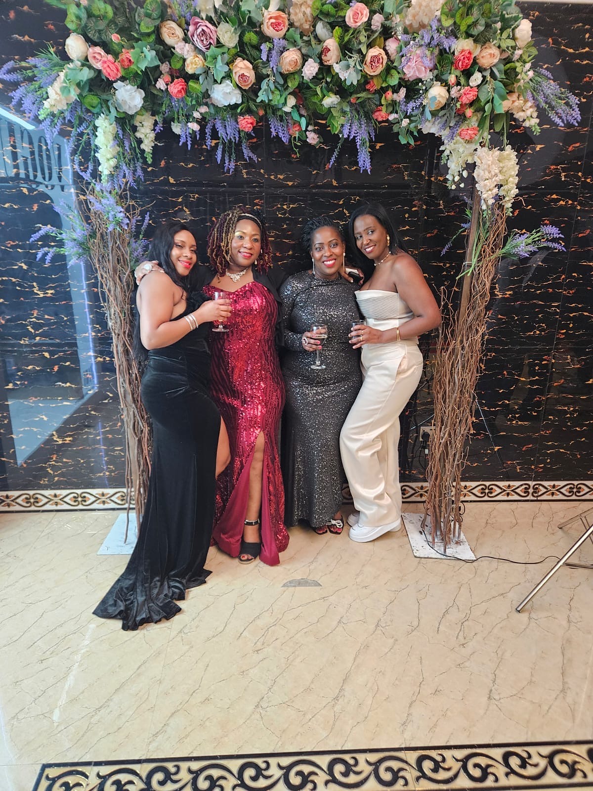 Three guests posing beneath a floral display at the 2024 Grille Community Christmas Gala